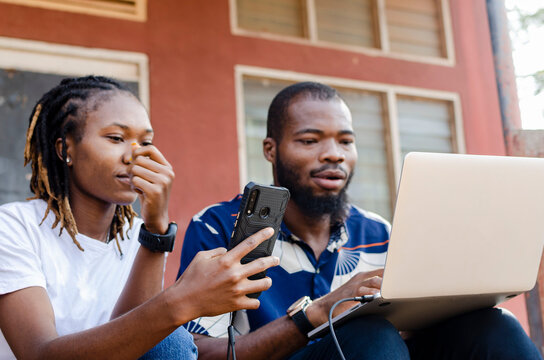 (phone in focus) - cropped picture of two africans sharing file from laptop to mobile phone