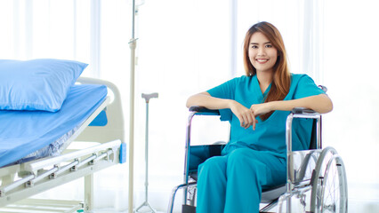 Portrait shot of young happy healthy Asian female patient in blue green hospital uniform sitting...