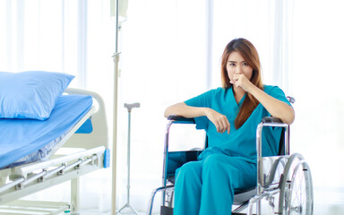 Portrait shot of young sick Asian female patient in blue green hospital uniform sitting alone...