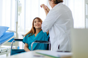 Obraz premium Old senior professional female doctor in white lab coat standing using stethoscope listening to heartbeat of disabled handicapped woman patient sitting on wheelchair in hospital checkup ward room