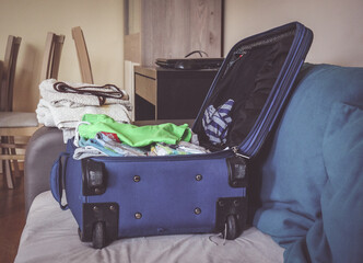 A closeup of a blue suitcase full of clothes lying on sofa ready before a trip