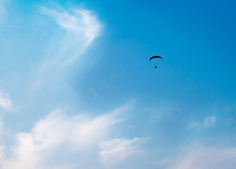 Parachutist soaring in a beautiful blue sky with light clouds. Paraglider - Feeling free on the sky