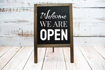 Sign of Welcome We are Open word on blackboard stand on wooden background