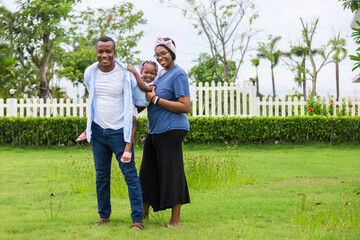 Happy family of African American people with young little daughter walking on green grass field...