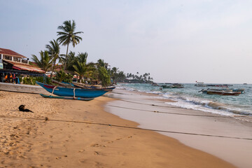 Fototapeta na wymiar Boat on the sand beach with palms and ocean waves.