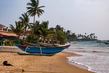Fototapeta na wymiar Boat on the sand beach with palms and ocean waves.