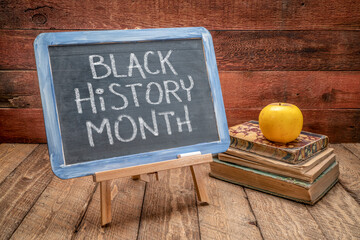 Black History Month, white chalk handwriting on a slate blackboard against rustic wood with books,...