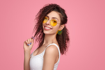 Stylish confident lady in trendy sunglasses smiling in pink studio