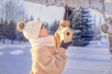 A cute boy in a white hat hangs a bird feeder on a tree.