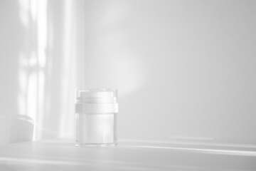 White plastic jar for packaging cosmetics in rays of sunlight. Close-up, monochrome background....
