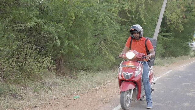 Delivery boy on scooter seraching for address by asking with customer on mobile phone - concept of deliveryman lifestyle, employment and communication