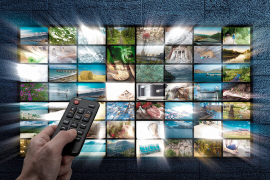 Online Multimedia video concept on TV set in dark room. Man watching online TV with remote control in hand. Multimedia streaming VoD content provider. Video on demand screen with remote control