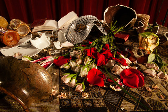 Still life Vanitas of red roses scattered on table with mask and broken dishes 
