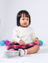Naklejka premium Studio shot of little cute short black hair Asian baby girl daughter model in casual plaid skirt sitting on floor smiling laughing playing with colorful round balls toy alone on white background
