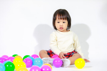Studio shot of little cute short black hair Asian baby girl daughter model in casual plaid skirt sitting on floor smiling laughing playing with colorful round balls toy alone on white background