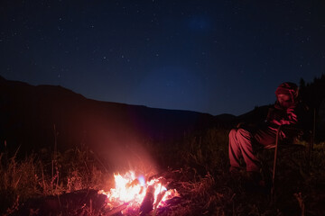 Woman is resting near fireplace at night time with night sky.