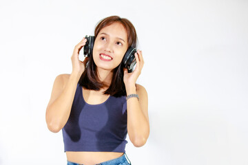 Naklejka premium Portrait isolated studio cutout shot of Asian young female model in crop top shirt and jeans holding big wireless headphone standing smiling look at camera listen to music songs on white background
