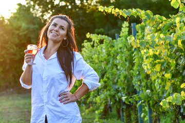 Young beautiful smiling woman  sitting with a cat in  a Vineyard with a glass of  rose wine. Woman playing with cat during the summer vacation