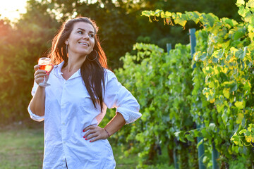 Young beautiful smiling woman  sitting with a cat in  a Vineyard with a glass of  rose wine. Woman playing with cat during the summer vacation