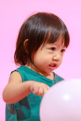 Fototapeta na wymiar Portrait studio shot little cute Asian kindergarten preschooler girl daughter model in casual long dress holding colorful balloons on pink background