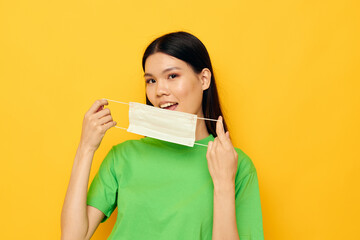 Fototapeta premium Portrait Asian beautiful young woman in green t-shirt medical mask protection yellow background unaltered