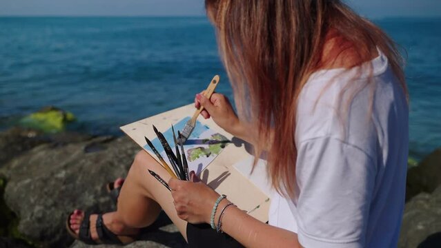 art therapy and meditation on seashore, woman is resting and painting marine landscape