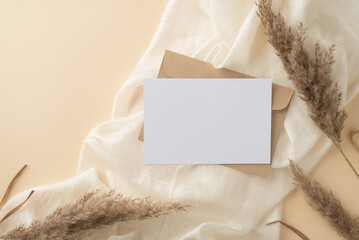 Top view photo of kraft paper envelope paper card white light scarf and pampas grass on isolated beige background with blank space