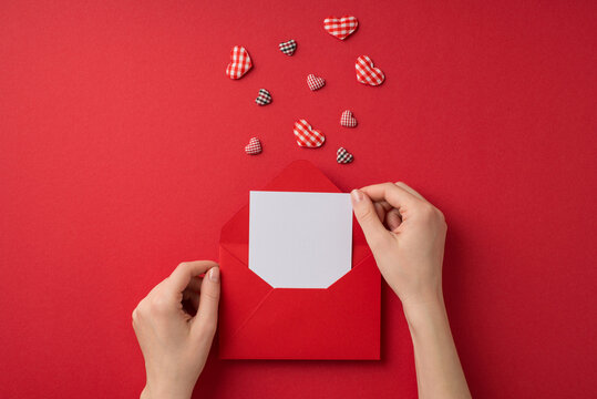 First Person Top View Photo Of Valentine's Day Decorations Female Hands Taking Letter Out Of Red Envelope And Checkered Hearts On Isolated Red Background With Blank Space