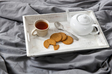 interior and home coziness concept. Top view. A cup of tea, a teapot with herbal tea, sugar bowl on a wooden tray on the bed. Porcelain cup
