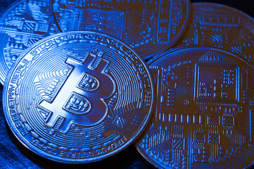 BTC coins in blue light on a dark background. Bitcoin cryptocurrency. Blockchain technology. Close-up.