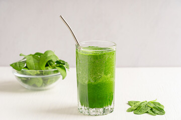 Green organic vegan homemade spinach smoothie or juice served in one drinking glass with straw and leaves ingredient on white wooden table at kitchen for breakfast. Healthy dieting concept