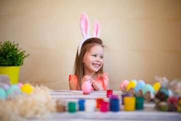 Happy little girl in bunnies ears prepares for Easter painted Easter eggs. Happy easter concept