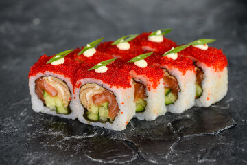 sushi roll stuffed with different fish with cucumber and cream cheese in red caviar on a black...