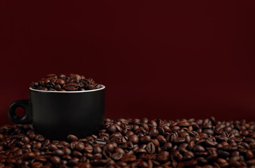 Roasted coffee beans on table and in cup opposite brown background. Copy Space
