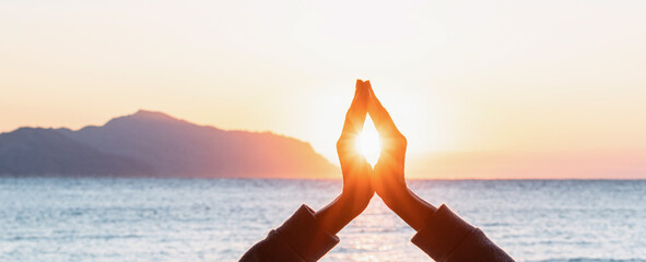 Closeup of hands in meditation pose with sun between them
