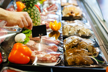 Male hand putting price tag on display of meat in shop, copy space