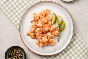 Grilled shrimps or tiger prawns served with lime, garlic and fresh herbs on scandi round plate on concrete surface. Pescatarian protein nutrition