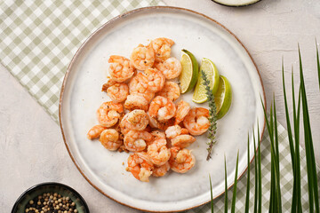 Grilled shrimps or tiger prawns served with lime, garlic and fresh herbs on scandi round plate on concrete surface. Pescatarian protein nutrition