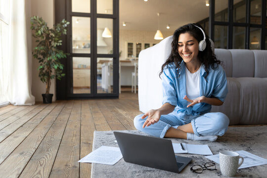 Portrait of cheerful Caucasian woman in headphones making video call, using laptop computer from home, free space