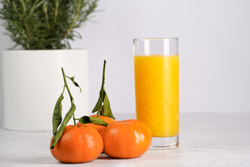Tall glass with orange mango smoothie, several tangerines on white surface