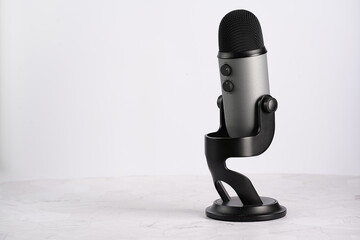 A grey microphone for podcasting or ASMR sounds on black sand on white surface, copy space