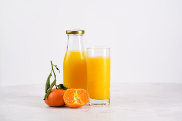 Tall glass with orange mango smoothie, several tangerines on white surface