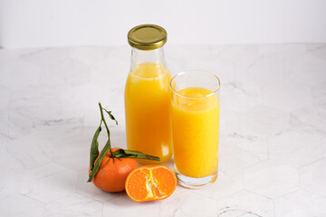 Tall glass with orange mango smoothie, several tangerines on white surface