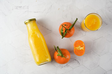 Tall glass with orange mango smoothie, several tangerines on white surface, top view flat lay