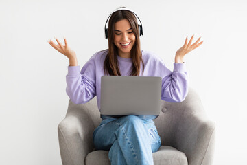 Happy Caucasian woman having web call on laptop, talking at camera while sitting in armchair on white background