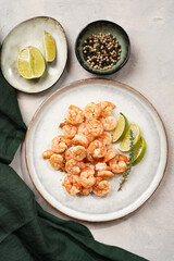 Grilled shrimps or tiger prawns served with lime, garlic and fresh herbs on scandi round plate on concrete surface. Pescatarian protein nutrition