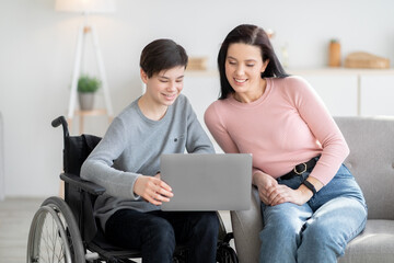 Home schooling. Handicapped teen boy in wheelchair learning online together with his mother indoors