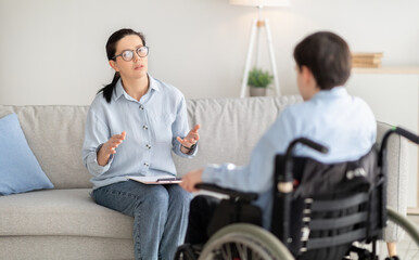 Psychotherapy for disabled teens. Young female psychologist speaking with teenage boy in wheelchair...