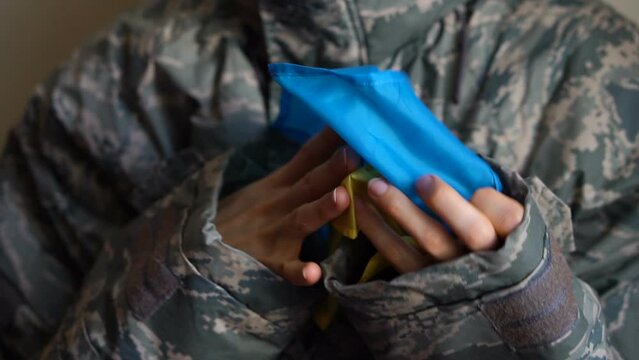 Young female soldier is holding ukrainian flag with love and anxiety due to escalation military conflict on the western part of Ukraine, Russian invasion, war concept