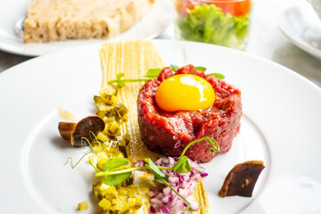 Traditional beef tartar served with a raw egg on top, onion and cucumber in white plate ready to be eaten